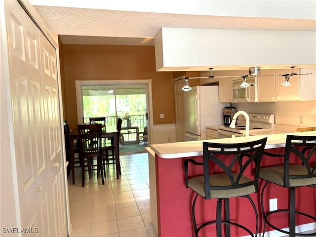 kitchen featuring kitchen peninsula, a textured ceiling, white appliances, a breakfast bar, and light tile patterned flooring