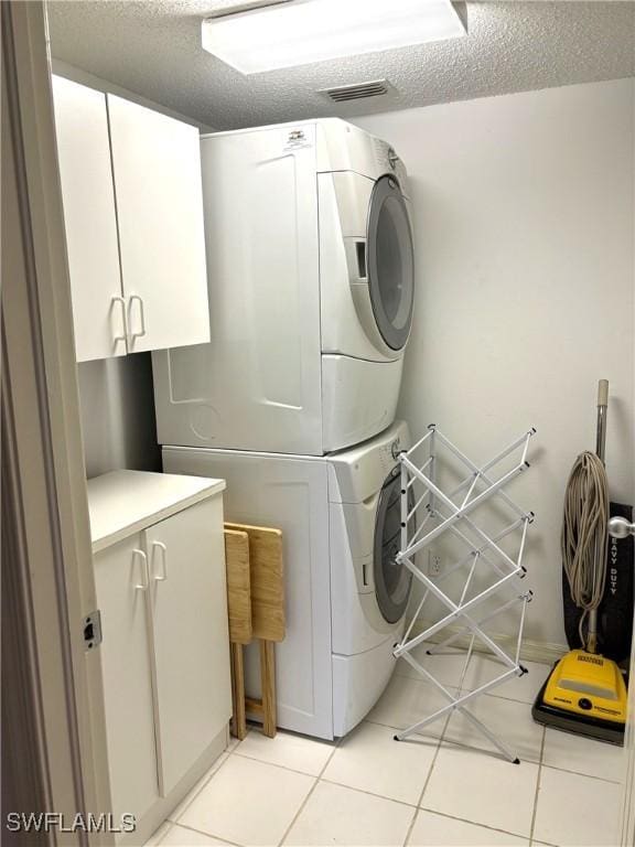 laundry room with cabinets, light tile patterned floors, a textured ceiling, and stacked washer and dryer