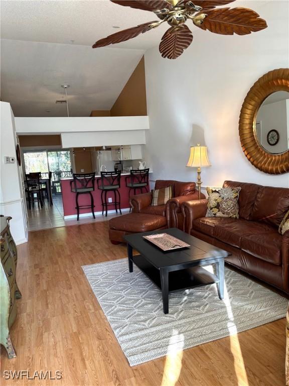 living room featuring ceiling fan, high vaulted ceiling, and light hardwood / wood-style floors