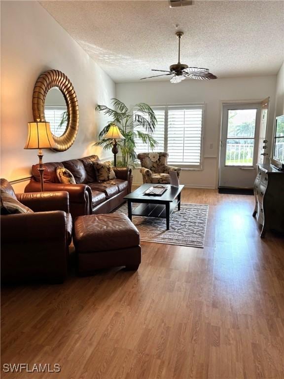 living room featuring wood-type flooring, ceiling fan, and a textured ceiling