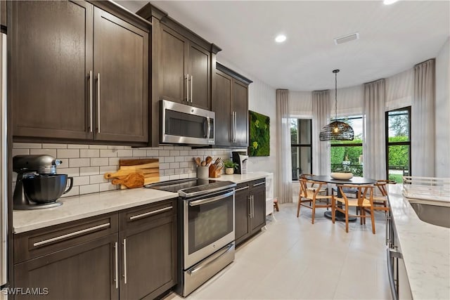 kitchen with pendant lighting, appliances with stainless steel finishes, tasteful backsplash, dark brown cabinets, and light stone counters