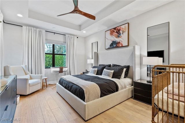 bedroom with a tray ceiling, ceiling fan, and light hardwood / wood-style floors