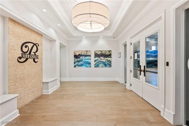 hallway featuring crown molding, light hardwood / wood-style flooring, a tray ceiling, and french doors