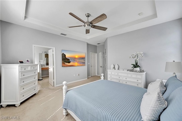 carpeted bedroom with a tray ceiling, ensuite bath, and ceiling fan