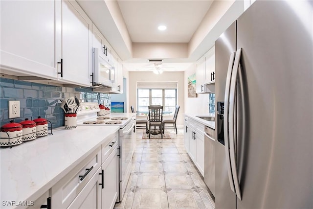 kitchen featuring appliances with stainless steel finishes, tasteful backsplash, light stone counters, ceiling fan, and white cabinetry