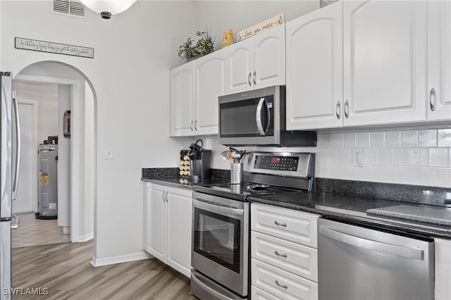 kitchen featuring appliances with stainless steel finishes, white cabinetry, tasteful backsplash, dark stone counters, and light wood-type flooring