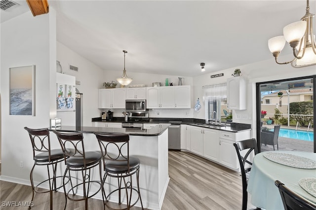 kitchen featuring lofted ceiling, sink, white cabinetry, decorative light fixtures, and appliances with stainless steel finishes