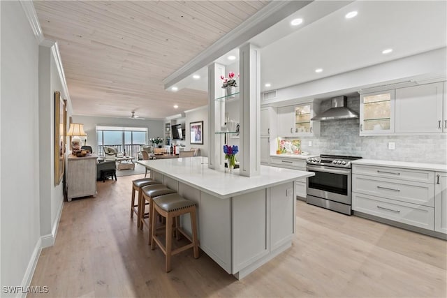 kitchen featuring stainless steel electric range oven, wall chimney exhaust hood, backsplash, white cabinetry, and a kitchen island