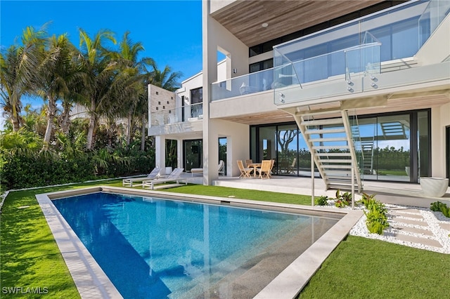 rear view of property featuring a lawn, a balcony, and a patio