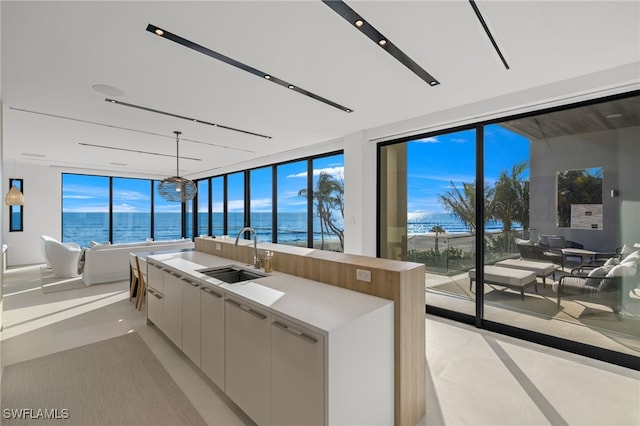 kitchen with white cabinetry, sink, light tile patterned floors, an island with sink, and a water view