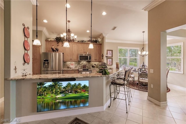 kitchen with kitchen peninsula, appliances with stainless steel finishes, light stone counters, an inviting chandelier, and a breakfast bar area