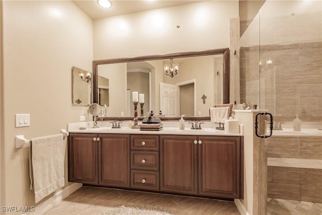 full bathroom featuring a sink, a notable chandelier, a stall shower, and double vanity