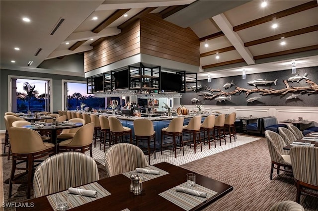 carpeted dining room with a towering ceiling, bar, and beam ceiling