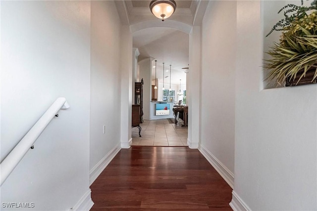 corridor with arched walkways, baseboards, and wood finished floors