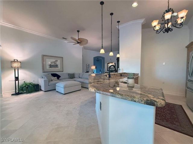 kitchen featuring ornamental molding, ceiling fan with notable chandelier, a sink, dark stone counters, and a peninsula