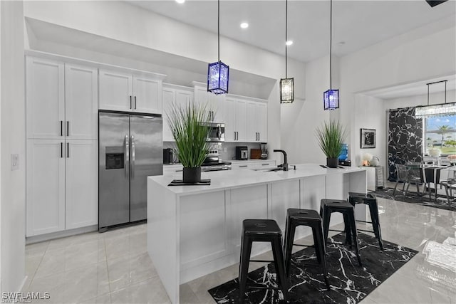 kitchen featuring white cabinets, decorative light fixtures, a kitchen island with sink, and appliances with stainless steel finishes