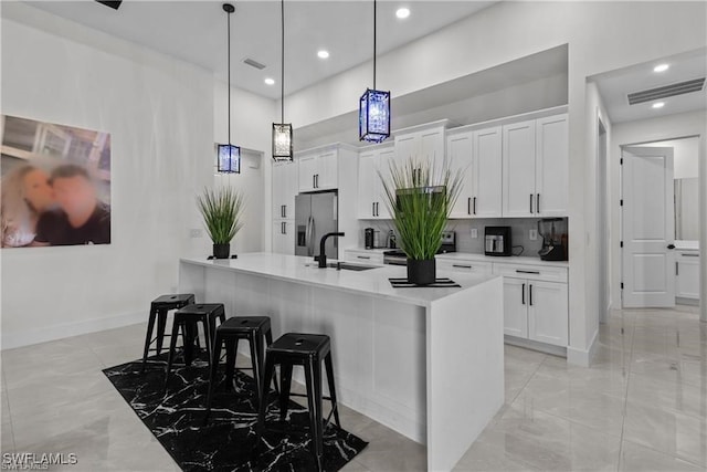 kitchen with sink, stainless steel fridge with ice dispenser, decorative light fixtures, a breakfast bar, and white cabinets