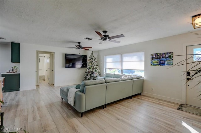 living room featuring ceiling fan, light hardwood / wood-style floors, and a textured ceiling