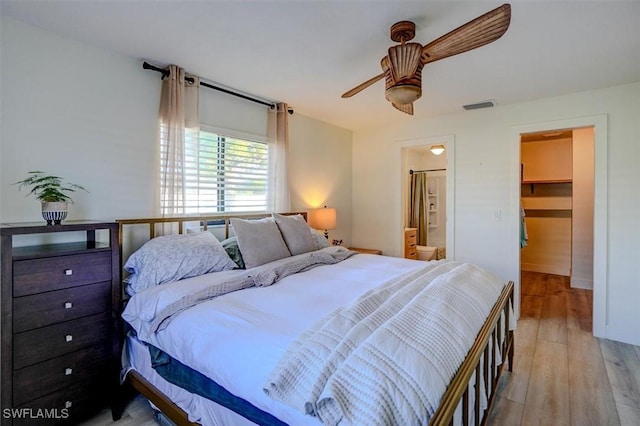 bedroom with a walk in closet, ceiling fan, light wood-type flooring, connected bathroom, and a closet