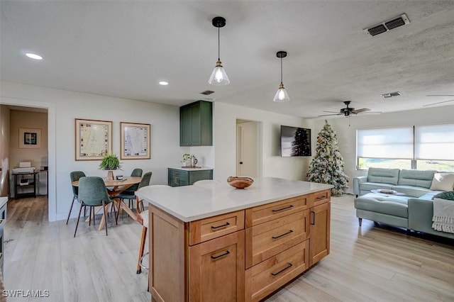 kitchen featuring light wood-type flooring, ceiling fan, pendant lighting, a kitchen island, and a breakfast bar area