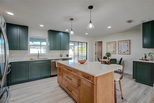 kitchen featuring stainless steel appliances, sink, pendant lighting, light hardwood / wood-style flooring, and a kitchen island