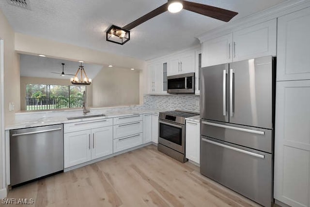 kitchen with white cabinets, appliances with stainless steel finishes, light countertops, a sink, and ceiling fan with notable chandelier