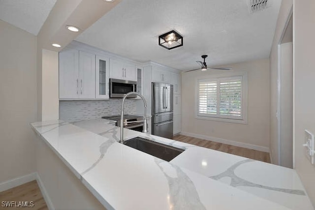 kitchen with visible vents, glass insert cabinets, a peninsula, stainless steel appliances, and white cabinetry