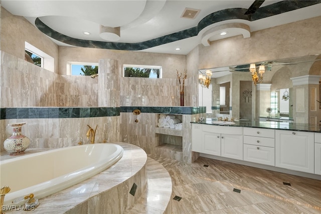 bathroom with vanity, tile walls, tiled tub, and an inviting chandelier