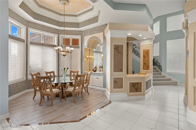 tiled dining space with a high ceiling, a tray ceiling, ornamental molding, and a notable chandelier