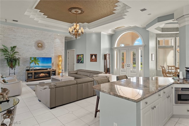 kitchen with light stone countertops, ornamental molding, a tray ceiling, light tile patterned floors, and white cabinets