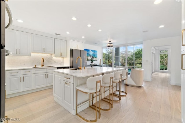 kitchen with a center island with sink, sink, plenty of natural light, light stone counters, and white cabinetry