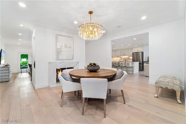 dining area with a chandelier, crown molding, a high end fireplace, and light hardwood / wood-style floors