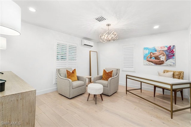 living area with light hardwood / wood-style flooring, a wall unit AC, and an inviting chandelier