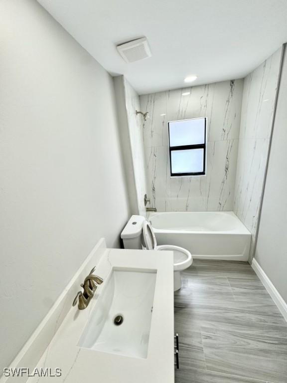 full bathroom featuring tiled shower / bath combo, toilet, and vanity