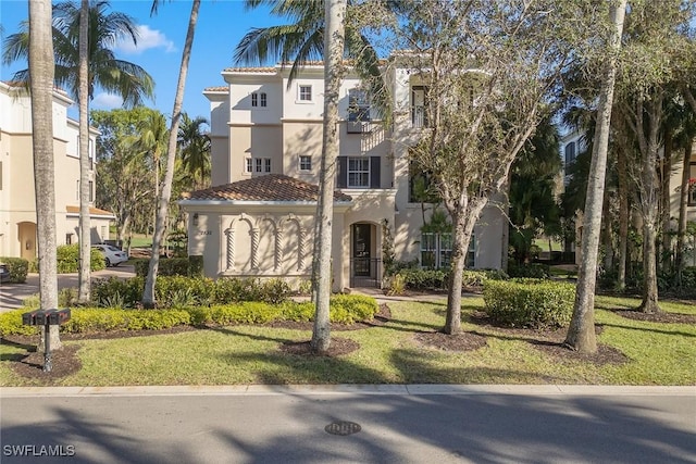 view of front of house featuring a front lawn, a tiled roof, an attached garage, and stucco siding