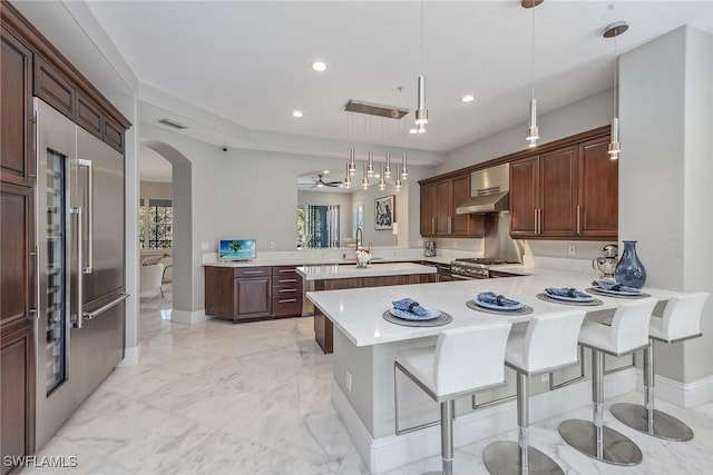 kitchen featuring a peninsula, arched walkways, light countertops, appliances with stainless steel finishes, and marble finish floor