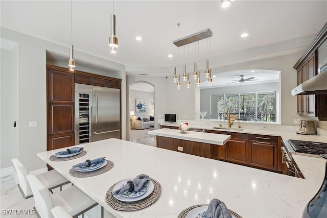 kitchen with stainless steel built in refrigerator, light stone counters, arched walkways, hanging light fixtures, and a sink