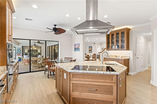 kitchen featuring light stone counters, light hardwood / wood-style flooring, island exhaust hood, an island with sink, and black electric cooktop