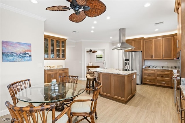 kitchen featuring light wood-type flooring, light stone counters, island range hood, stainless steel appliances, and a center island