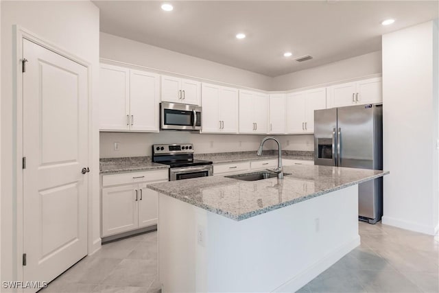 kitchen featuring white cabinets, a center island with sink, sink, light stone counters, and stainless steel appliances