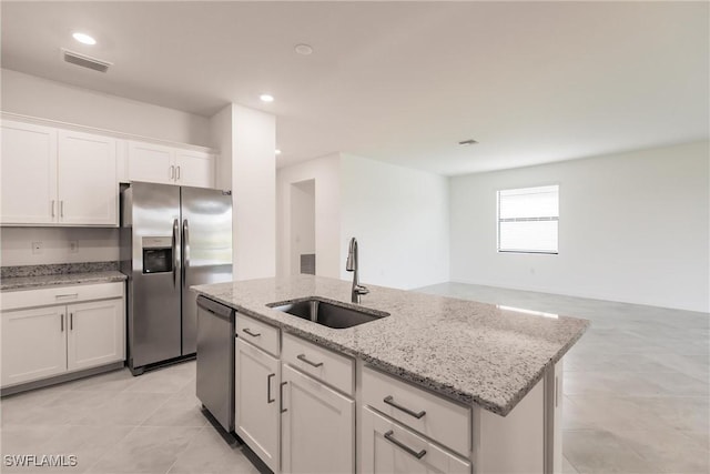 kitchen featuring a center island with sink, sink, light stone counters, white cabinetry, and stainless steel appliances