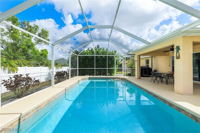 view of swimming pool featuring glass enclosure, ceiling fan, and a patio