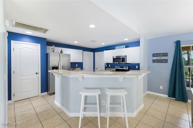 kitchen with light tile patterned floors, white cabinetry, a breakfast bar area, and appliances with stainless steel finishes