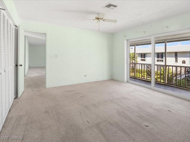 empty room featuring ceiling fan, light carpet, and a textured ceiling