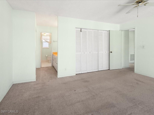 unfurnished bedroom with ceiling fan, light colored carpet, ensuite bathroom, and a closet