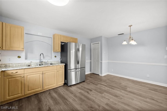 kitchen with stainless steel refrigerator, sink, hanging light fixtures, an inviting chandelier, and hardwood / wood-style floors