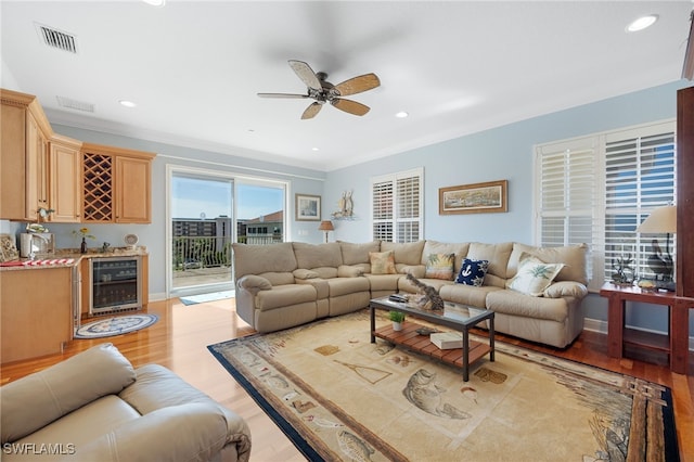 living room featuring ceiling fan, light wood-type flooring, ornamental molding, and beverage cooler