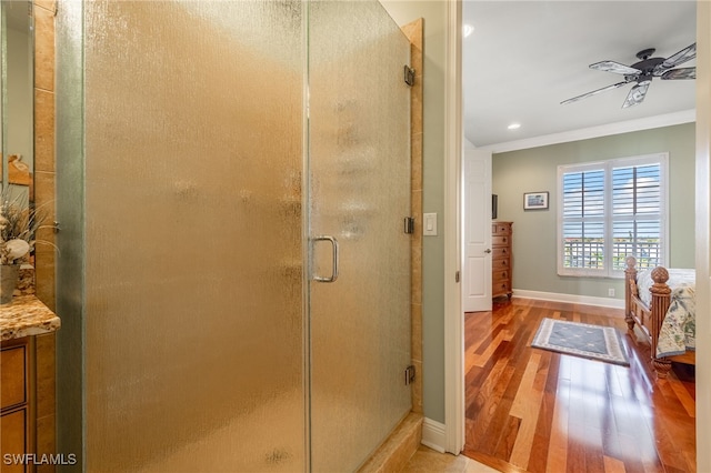 bathroom with wood-type flooring, a shower with door, ornamental molding, and ceiling fan