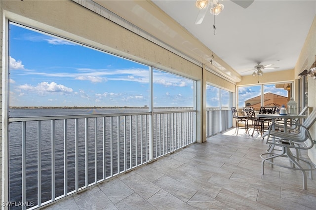 unfurnished sunroom featuring ceiling fan and a water view