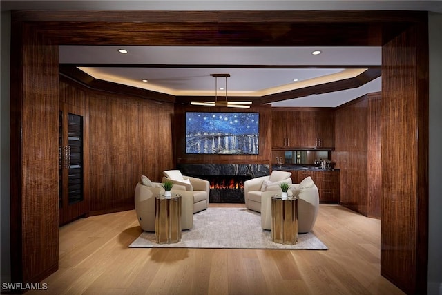 cinema with a premium fireplace, wood walls, light wood-type flooring, and a tray ceiling